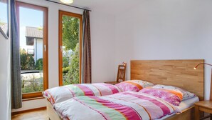 A bedroom with a wooden bed, a nightstand, and a window with curtains. - Holiday Apartment "Oestreich" close to Chiemsee Lake with Wi-Fi & Terrace (Chieming/ Egerer)