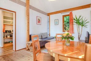 Un intérieur moderne avec une table à manger en bois, un canapé et un coin cuisine visible à travers une porte ouverte.