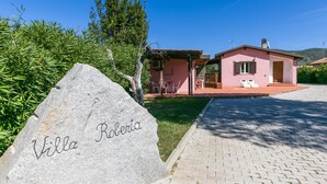 Una villa llamada 'Villa Roberta' con un camino de entrada pavimentado, un pequeño jardín y un edificio rosa con mobiliario exterior.