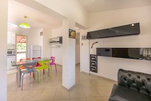 A modern kitchen with a glass dining table, colorful chairs, a black leather sofa, and a built-in stove.