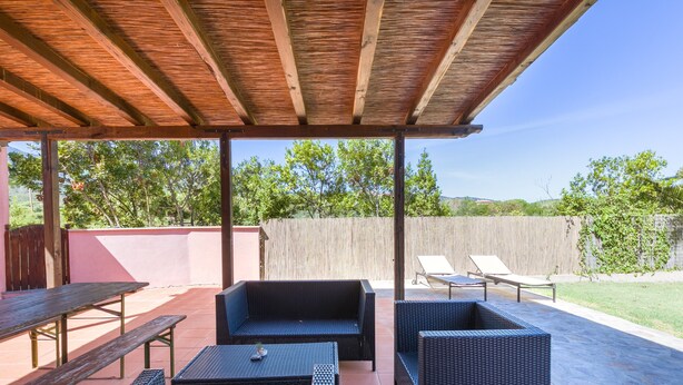 Un patio al aire libre con una pérgola de madera, un sofá de mimbre negro, una mesa de comedor y una silla de descanso.