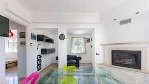 Una sala de estar moderna con una mesa de comedor de vidrio, un sofá de cuero negro, una chimenea y un televisor montado en la pared.