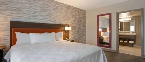 A hotel room with a large bed, a nightstand, a wall-mounted lamp, and a bathroom visible through an open door.