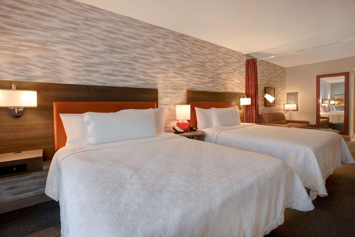 Une chambre d’hôtel avec deux lits, chacun doté d’une tête de lit en bois, de draps blancs et de lampes de chevet.