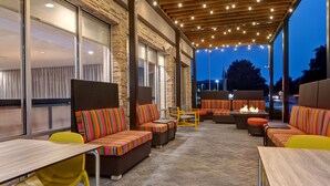 An outdoor patio with wicker furniture, a fire feature, and string lights. - Home2 Suites by Hilton Carmel Indianapolis (Carmel)