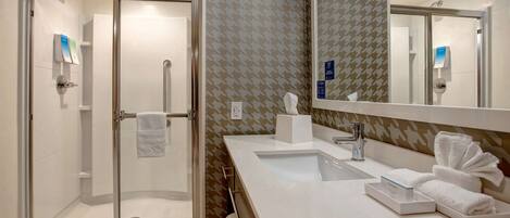 A modern bathroom with a glass-enclosed shower, a large mirror, and a white sink with a towel rack.