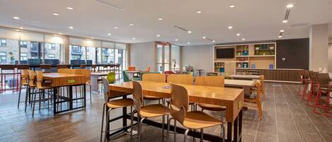 A spacious dining area with multiple tables and chairs, large windows, and a modern kitchen area.