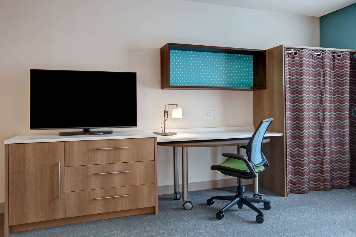 Une pièce comprenant un bureau, un téléviseur, une chaise et un rideau.