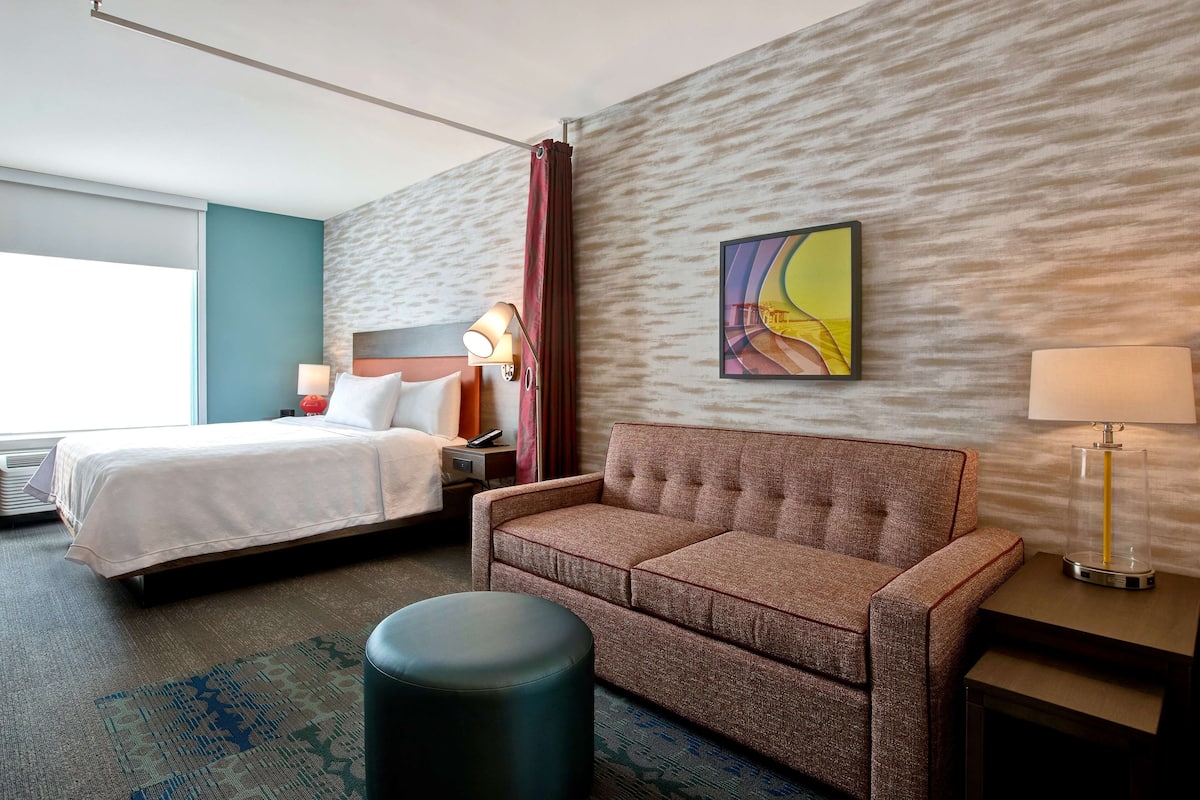 Une chambre d’hôtel avec un lit, un canapé, une petite table, une lampe et un tableau au mur.
