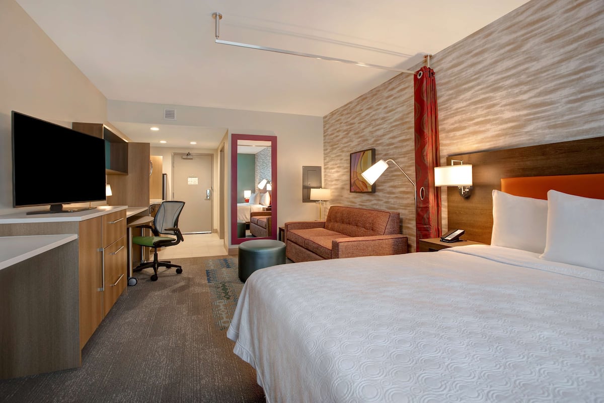 Une chambre d’hôtel avec un lit, un bureau doté d’une télévision, une chaise, une lampe et une salle de bain visible à travers une porte ouverte.