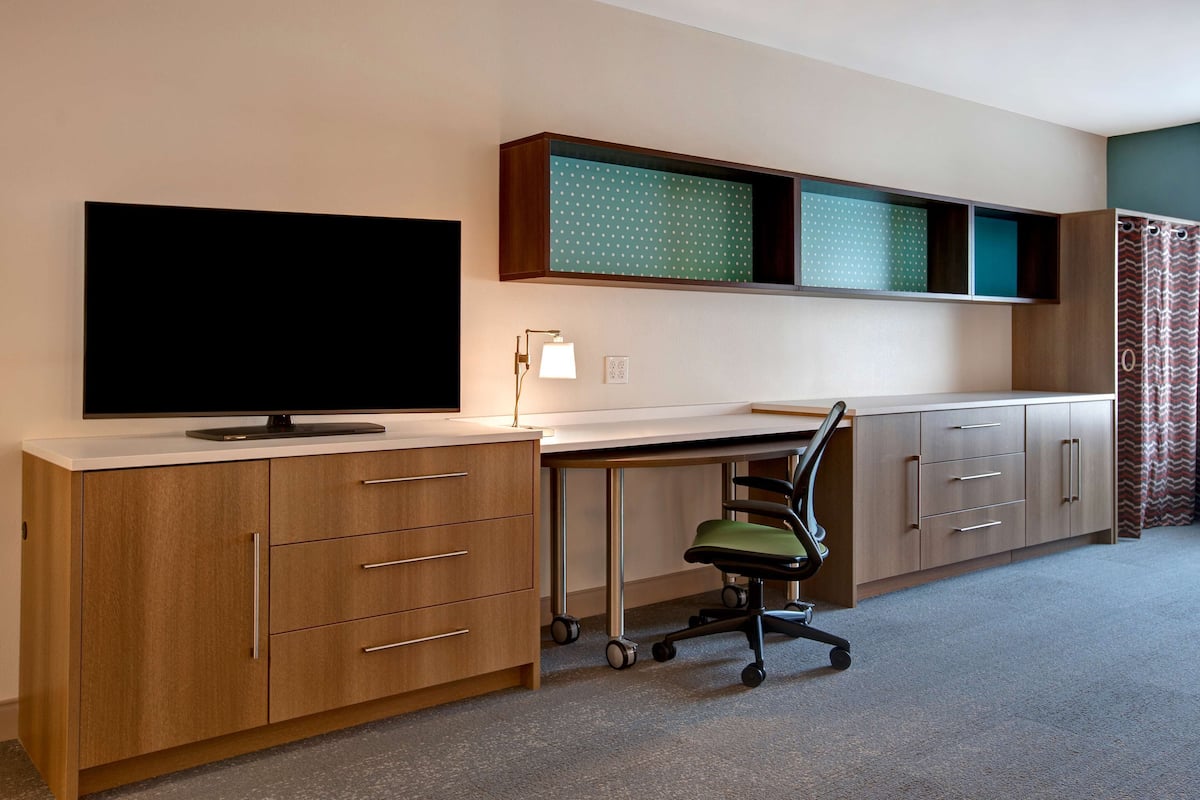 Un espace de bureau moderne équipé d’un téléviseur à écran plat, d’un bureau, d’une chaise et d’un meuble avec des tiroirs.