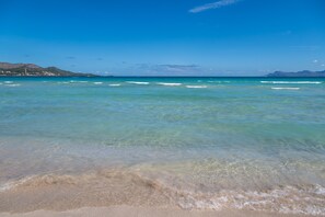 Uma praia com águas cristalinas, montanhas ao longe e um céu limpo.