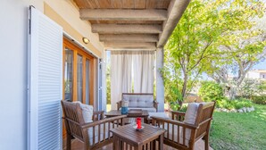 Eine Terrass mit einer Couch, zwei Holzstühlen, einem Tisch und einer Glastür.