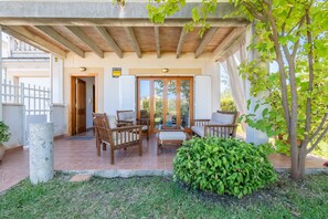 Un espace extérieur abrité, aménagé avec du mobilier en bois, un pilier en pierre et un pot de fleurs.
