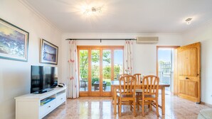 Ein Wohnzimmer mit Fernseher, Esstisch, Stühlen und einer Glastür zum Außenbereich.