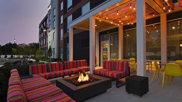 An outdoor seating area with colorful striped sofas and chairs, a fire pit, and a covered patio with string lights.