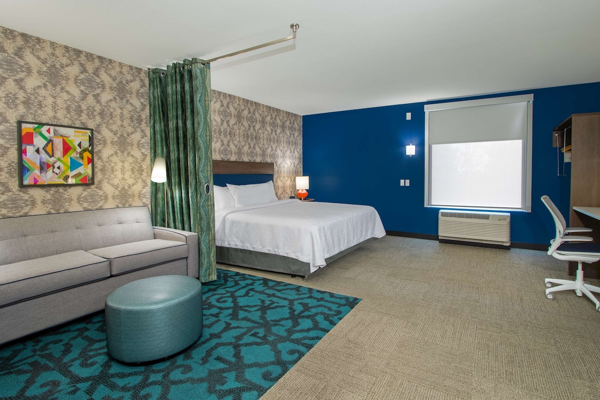 Een hotelkamer met een bed, een bank, een rond poefje, een bureau en een stoel.