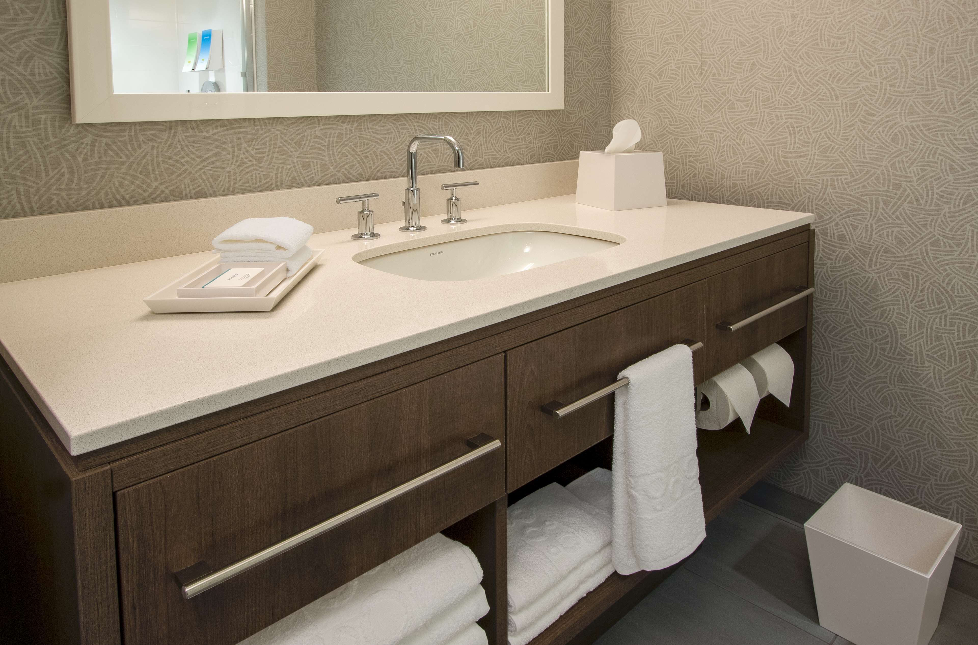 Une salle de bain équipée d’un lavabo, d’un miroir, d’un porte-serviettes et d’une poubelle.