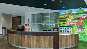 A hotel reception area with a wooden reception desk, a large window, and a colorful mural depicting a town scene.