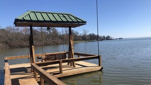 A wooden dock with a bench and a covered area, extending into a calm lake.