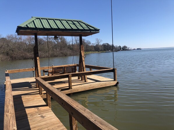 A wooden dock with a bench and a covered area, extending into a calm lake.