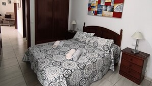 A bedroom with a bed, a nightstand, a wooden wardrobe, a wall art piece, and a ceiling light.