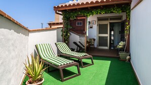 A patio with two striped lounge chairs, a green artificial turf floor, and a potted plant.