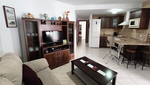 A living room with a sofa, a coffee table, a TV, and a kitchen area with a refrigerator and a microwave.