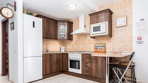 A kitchen with wooden cabinets, a white refrigerator, a microwave, a stove, and a dining area with a table and chairs.