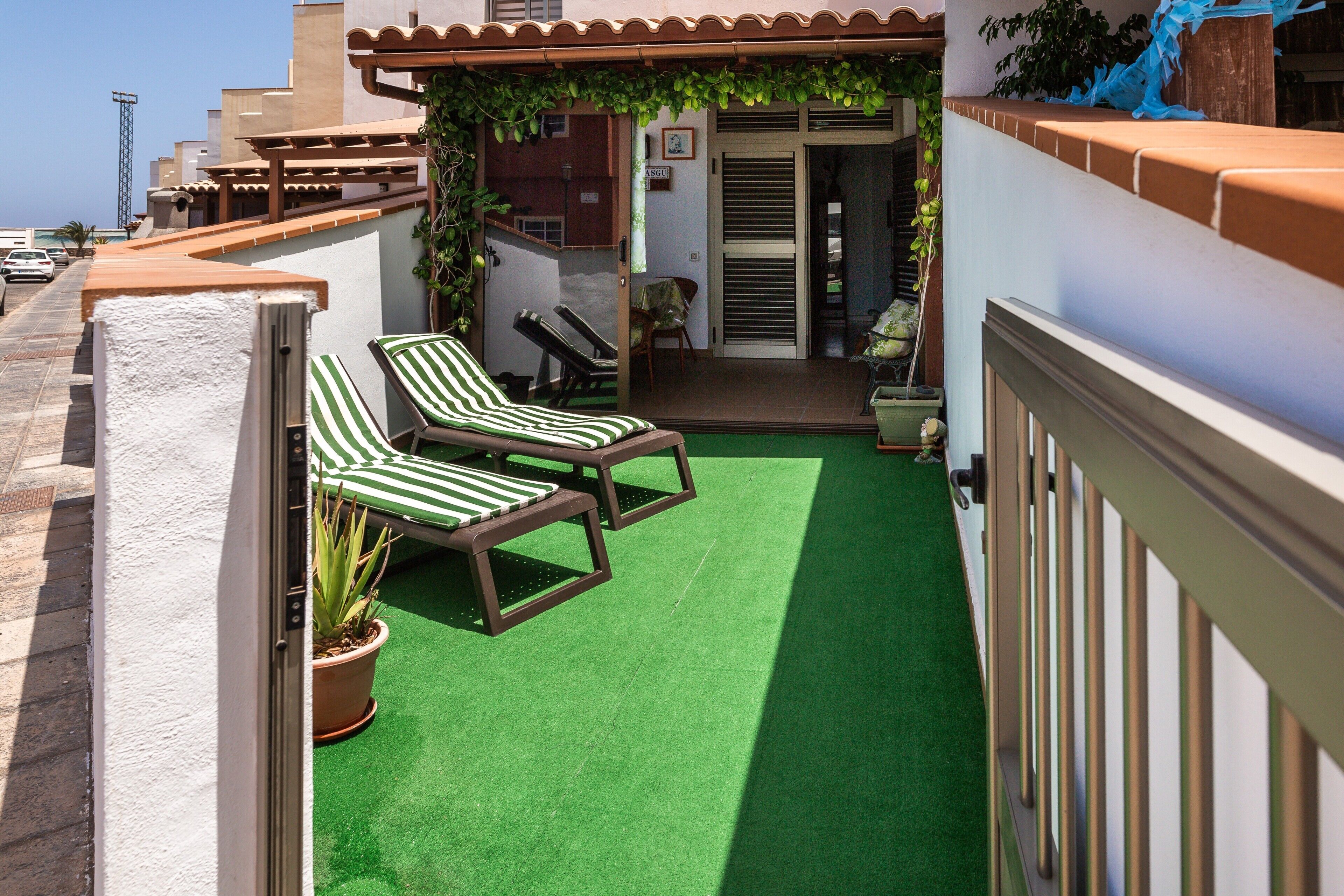Une terrasse sur le toit, recouverte de gazon synthétique, avec deux chaises longues, un pot de fleurs et une vue sur les bâtiments environnants.