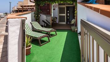 Une terrasse sur le toit, recouverte de gazon synthétique, avec deux chaises longues, un pot de fleurs et une vue sur les bâtiments environnants.