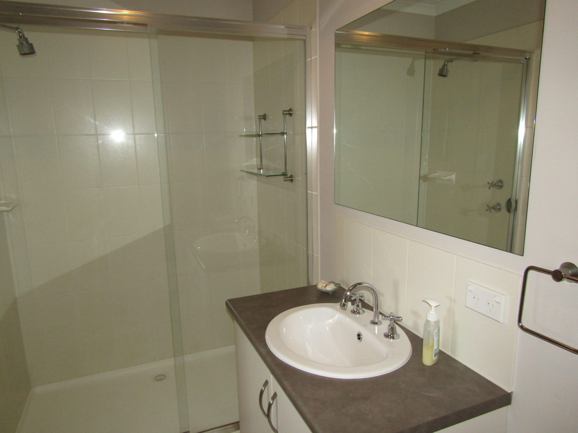 A bathroom with a glass shower enclosure, a white sink with a brown countertop, and a mirror above the sink.