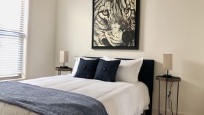 Un dormitorio con una cama grande, dos mesitas de noche, un cuadro colgado en la pared y una ventana con persianas.