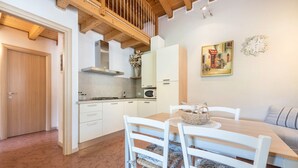 Una cocina con armarios blancos, techo de madera y una zona de comedor con sillas y mesa blancos.