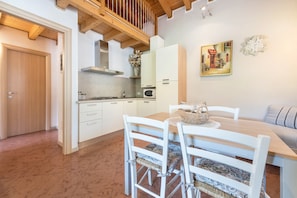 Una cocina con armarios blancos, techo de madera y una zona de comedor con sillas y mesa blancos.