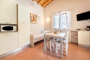 Cocina compacta con microondas, una mesa de comedor con sillas, un sofá y un televisor montado en la pared.