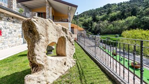 Una estructura de piedra con un arco, un balcón con barandilla y vistas a un paisaje verde con árboles.