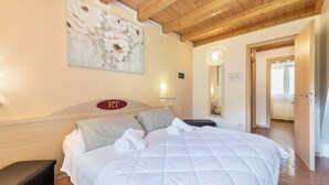 Habitación de hotel con cama, cabecero con logotipo, un cuadro en la pared, un espejo y una puerta que da a otra habitación.