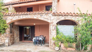 A two-story building with a stone facade, an outdoor dining area with chairs and a table, and a covered entrance. - Holiday Apartment "Runcina 2" with Sea View in Green Landscape (san teodoro)