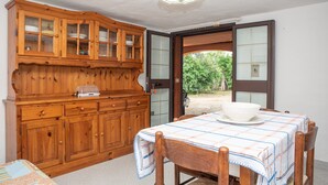 A dining area with a wooden cabinet, a table with a tablecloth, and a view through an open door. - Holiday Apartment "Runcina 2" with Sea View in Green Landscape (san teodoro)
