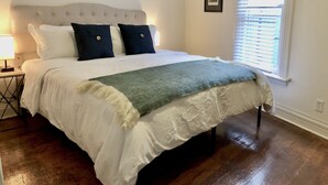 A neatly made bed with a white duvet, two dark pillows, and a green throw blanket. - NEW! Hip Downtown Pad! Walk Everywhere! (Hot Springs)