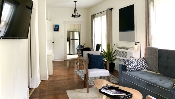 A modern living room with a grey sofa, a coffee table, and a TV mounted on the wall. - NEW! Hip Downtown Pad! Walk Everywhere! (Hot Springs)
