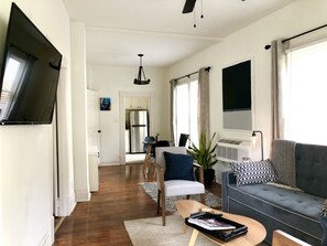 A modern living room with a grey sofa, a coffee table, and a TV mounted on the wall. - NEW! Hip Downtown Pad! Walk Everywhere! (Hot Springs)