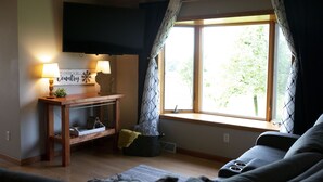 Una sala de estar con una mesa de madera, un sofá, un televisor montado en la pared y un ventanal con cortinas.
