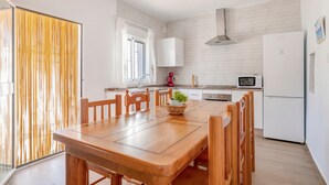 A modern kitchen with white brick walls, a wooden dining table, and a refrigerator. - Charming Home with Pool, Large Lawn, Patios & Wi-Fi; Parking Available, Pets Allowed (Conil de la frontera)