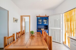 Un comedor con una mesa de madera, sillas, un armario azul con puertas de cristal y vistas a través de un ventanal.