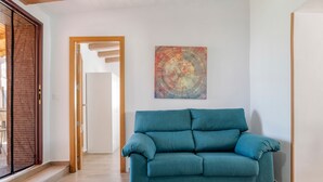 A teal sofa in a hallway with a wooden door frame, a colorful abstract painting on the wall, and a wooden floor. - Charming Home with Pool, Large Lawn, Patios & Wi-Fi; Parking Available, Pets Allowed (Conil de la frontera)