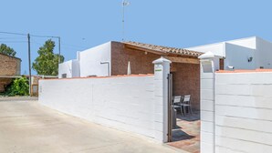 A gated entrance with a white wall, a brick building with a tiled roof, and a clear sky. - Charming Home with Pool, Large Lawn, Patios & Wi-Fi; Parking Available, Pets Allowed (Conil de la frontera)