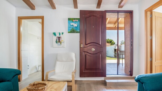 A room with a wooden door, a white chair, a wooden table, and a green sofa. - Charming Home with Pool, Large Lawn, Patios & Wi-Fi; Parking Available, Pets Allowed (Conil de la frontera)