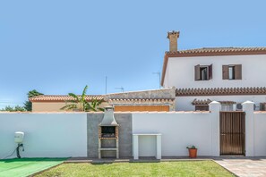 Una casa con una barbacoa de ladrillo, un muro blanco, un portón y un pequeño jardín.